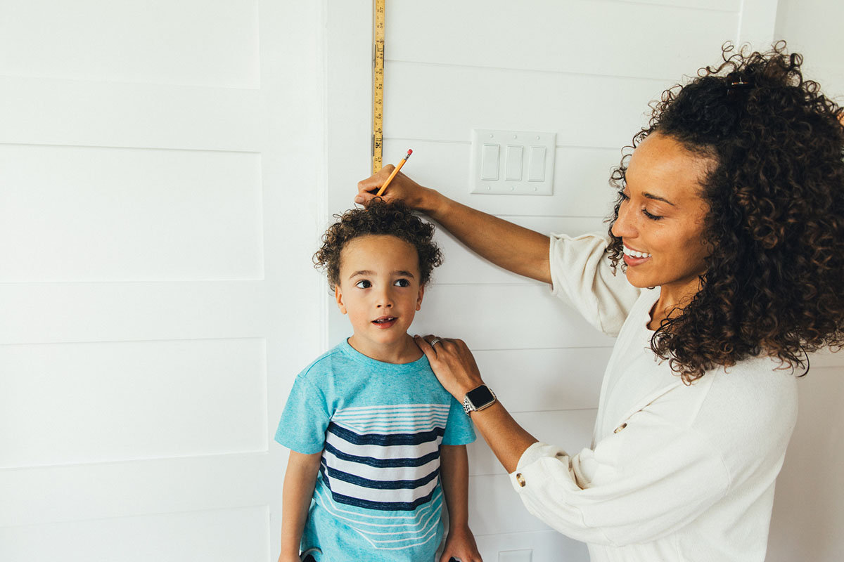 Mother measuring boy standing next to ruler