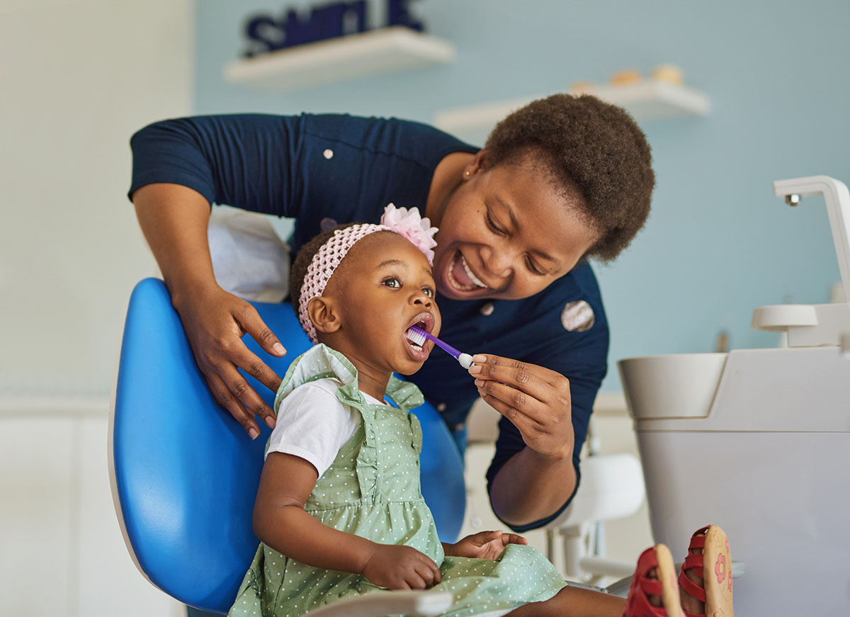 Woman helping young child brush her teeth