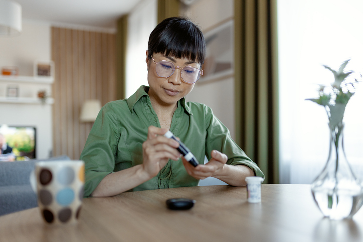 Asian Woman Using a Glucose Monitoring Device at Home