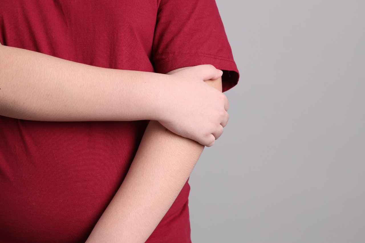 A child wearing a red shirt holds the back of their arm, covering it